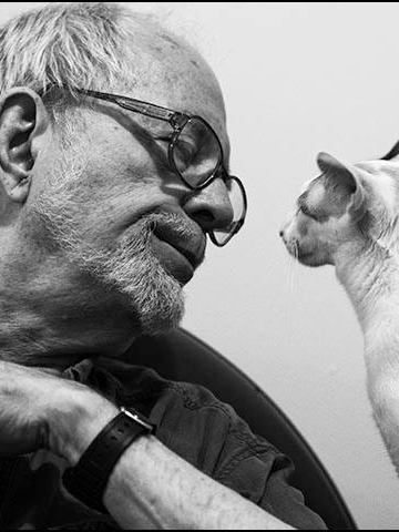 David McReynolds on the left, looks at a cat on the right.
