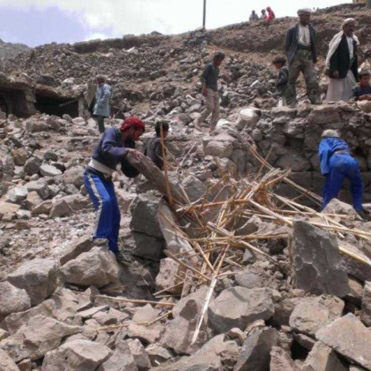 Around a dozen people climb over the rubble of demolished buildings in Yemen.